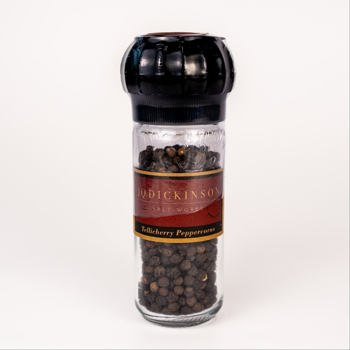 Pepper grinder with black peppercorns and a visible label on a white background